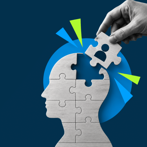 Head silhouette made of puzzle pieces; a hand places a missing piece with a person icon into the head, against a blue background.